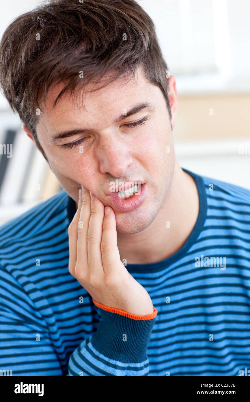 Porträt eines Mannes mit tobenden Zahnschmerzen im Wohnzimmer sitzen Stockfoto