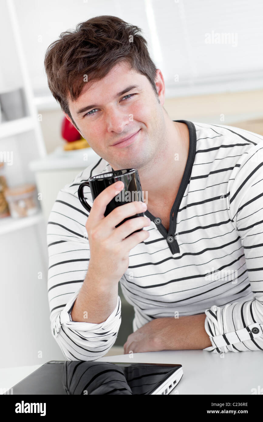 Kluger Mann hält eine Tasse Kaffee mit seinem Laptop auf dem Tisch in der Küche Stockfoto