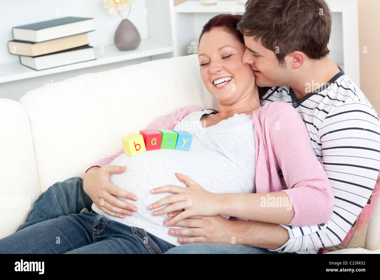 Porträt einer glücklichen schwangeren Frau mit Baby auf dem Bauch und ihres Mannes, küsste sie auf eine Stockfoto