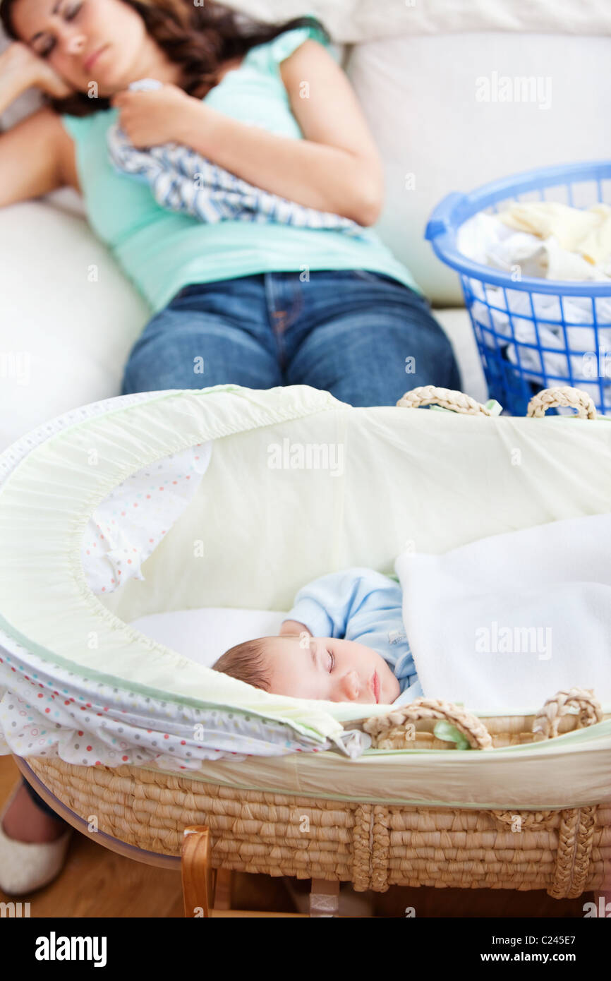 Niedliche Baby schlafend in seiner Wiege mit seiner Mutter auf der Couch im Hintergrund Stockfoto