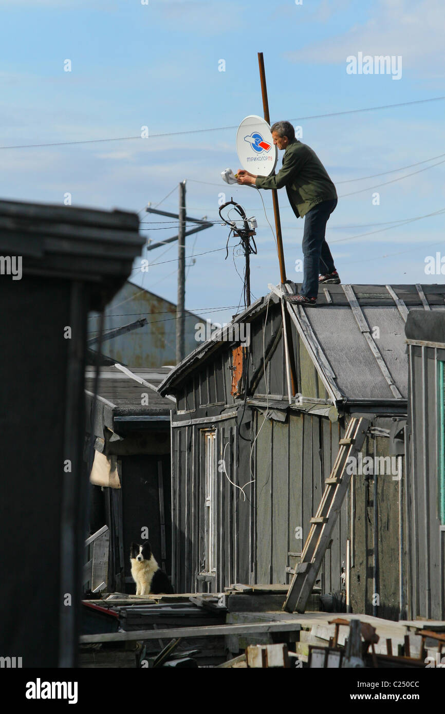 Mann montieren Schüssel Sat-TV auf seinem Dach. Siedlung Mys-Stein, Jamal-Halbinsel, Russland Stockfoto