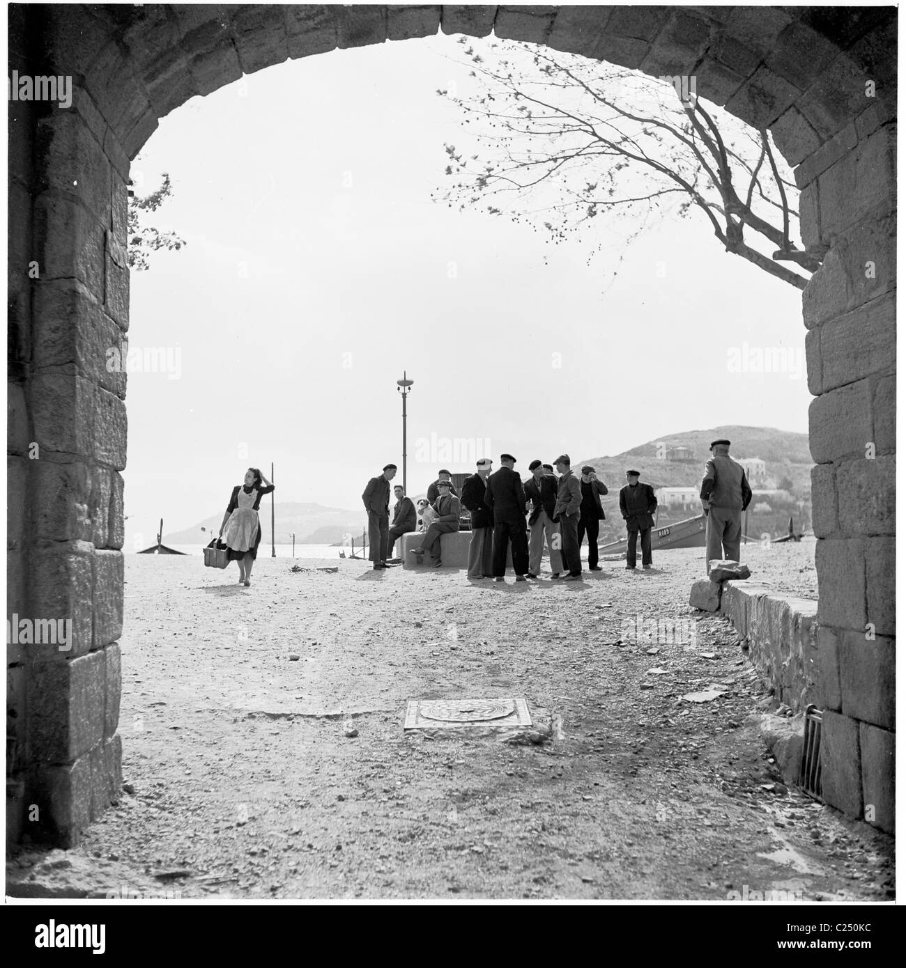 1950s. Blick durch den alten Torbogen von Menschen, die sich auf rauem Land in der mediterranen Stadt Collioure, Frankreich, versammeln. Stockfoto