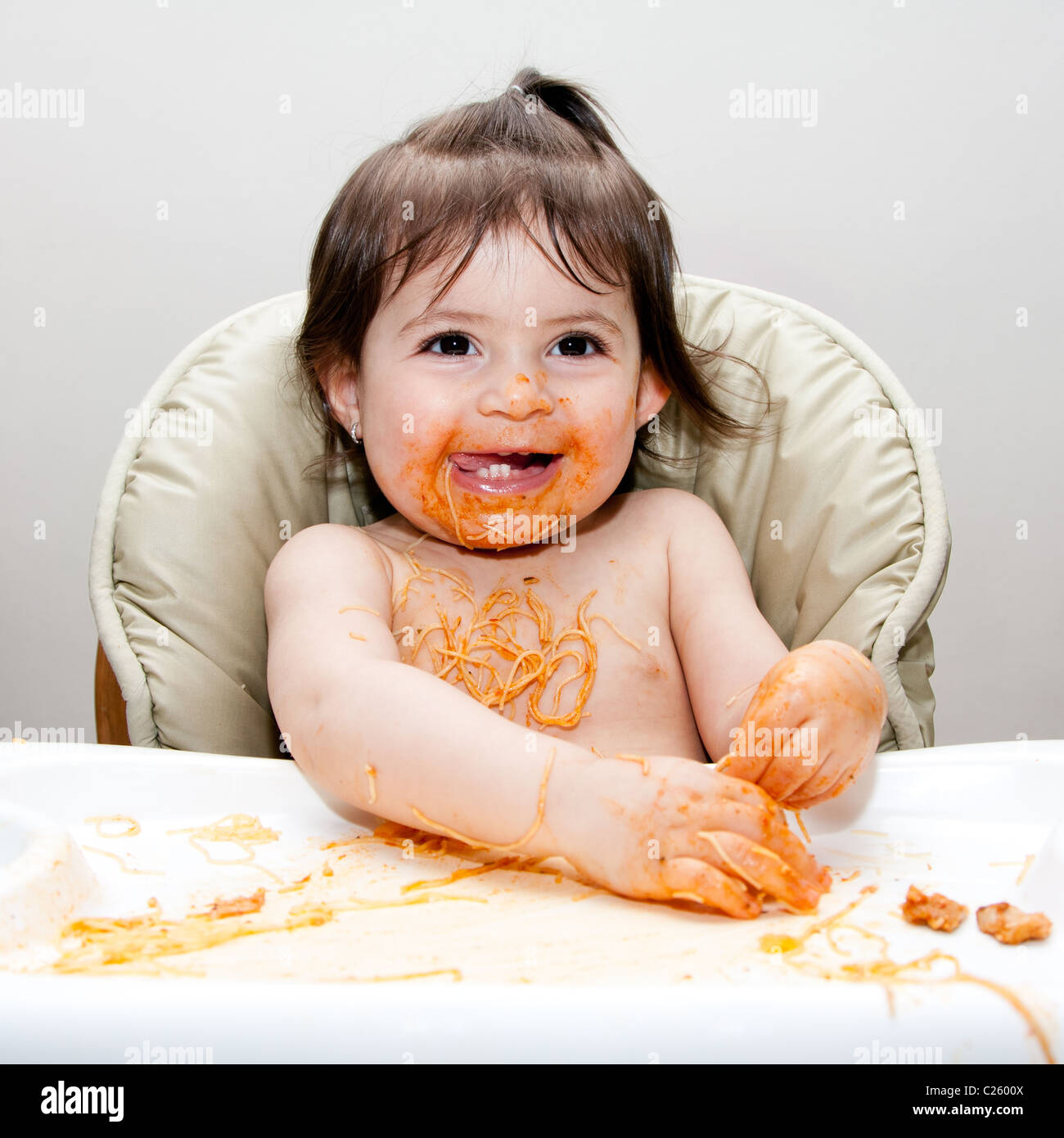 Glückliches Baby Spaß Essen chaotisch bedeckt in Angel Hair Pasta Spaghetti rot marinara Tomatensauce. Stockfoto