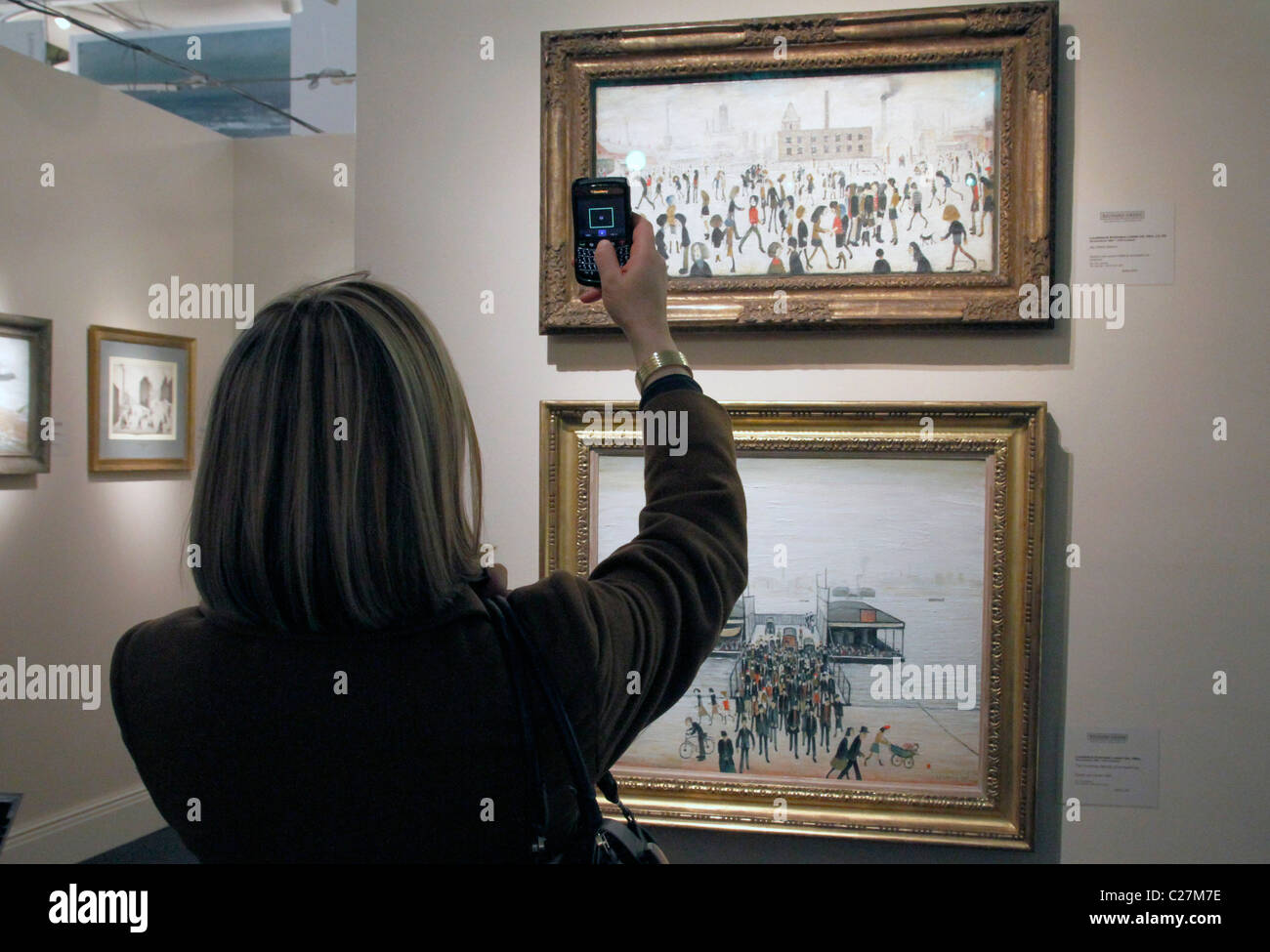 FRAU FOTOGRAFIEREN MALEREI VON L.S. LOWRY AUF EINER KUNSTMESSE IN LONDON Stockfoto