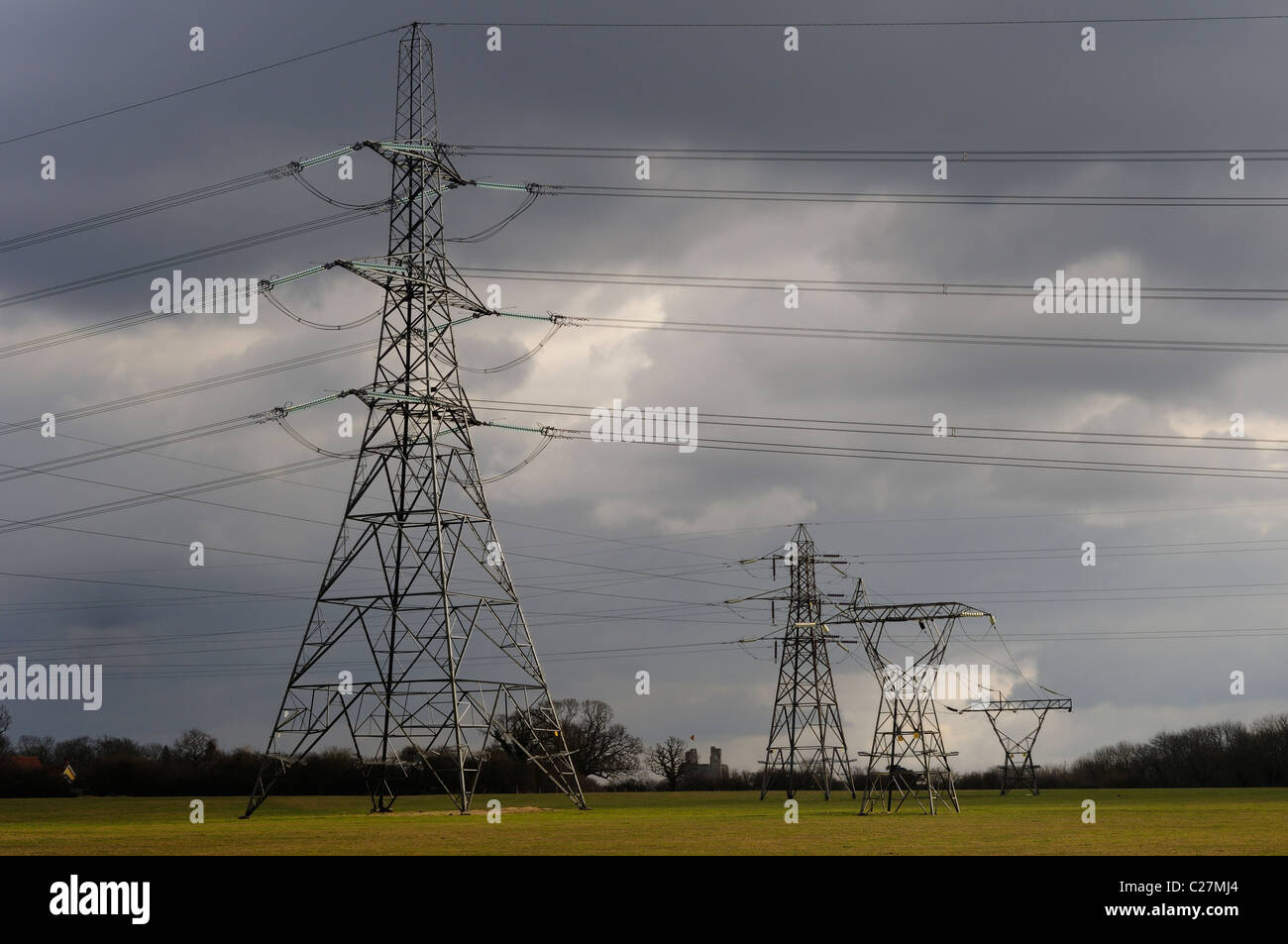 Strommasten und ihre Stromkabel überqueren ein Feld unter einem dunklen bewölkten Himmel. Stockfoto