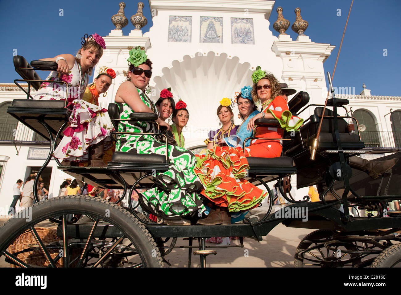 Frauen in Flamenco-Kleider fahren eine Kutsche vor der Liebfrauenkirche in El Rocio, während die jährliche Wallfahrt. Stockfoto