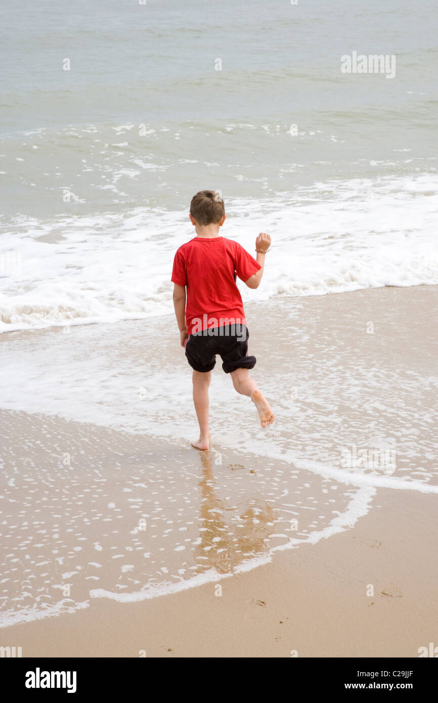 Jungen spielen am Ufer Meeres, die ankommenden Flutwellen auszuweichen. Meer Palling, Norfolk. Stockfoto