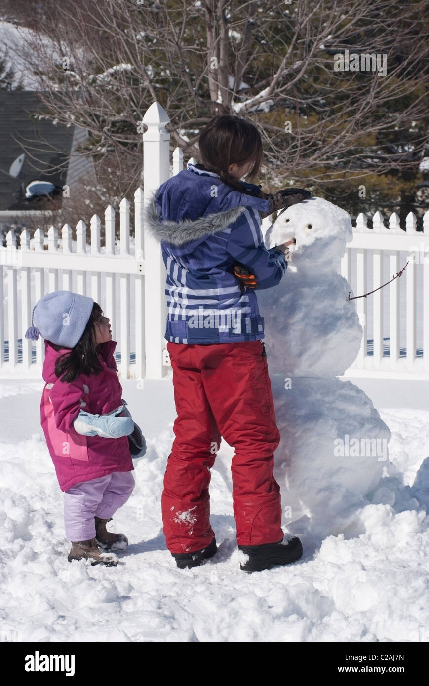 12-Year-Old und ihre drei-jährige Schwester bauen einen Schneemann außerhalb ihrer Heimat Pennsylvania. Stockfoto