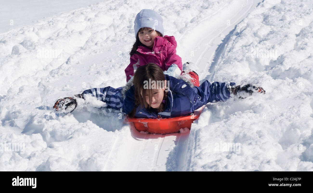 Drei-jährige reitet auf ihrer älteren Schwester zurück, als sie einem schneebedeckten Hügel in der Nähe von Pittsburgh, Pennsylvania rutschen. Stockfoto