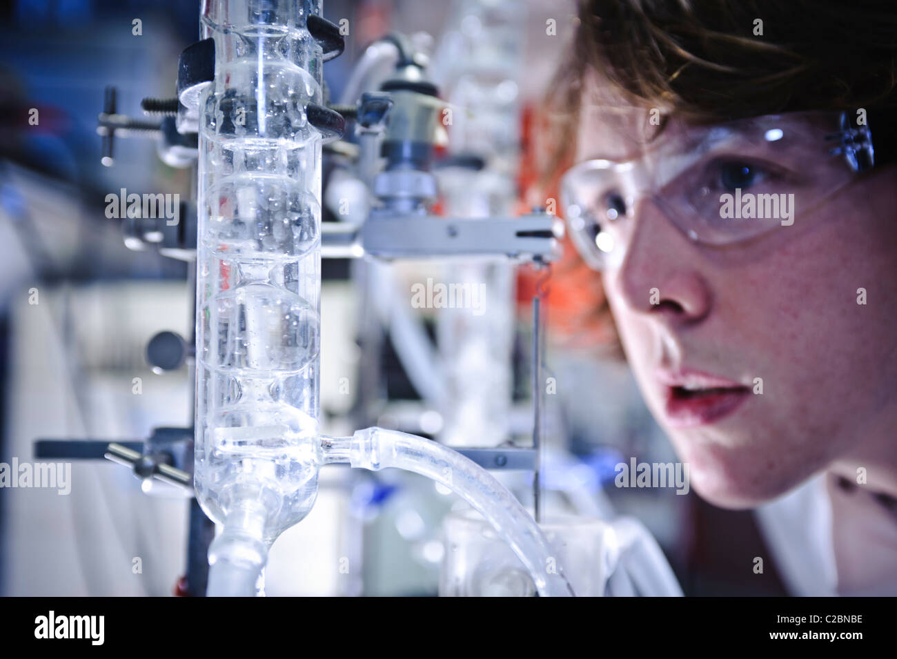 Junge männliche Wissenschaftler tragen Brille betrachten intensiv und klare Flüssigkeit wirbelnden in großen Glasröhre im Wissenschaftslabor Stockfoto