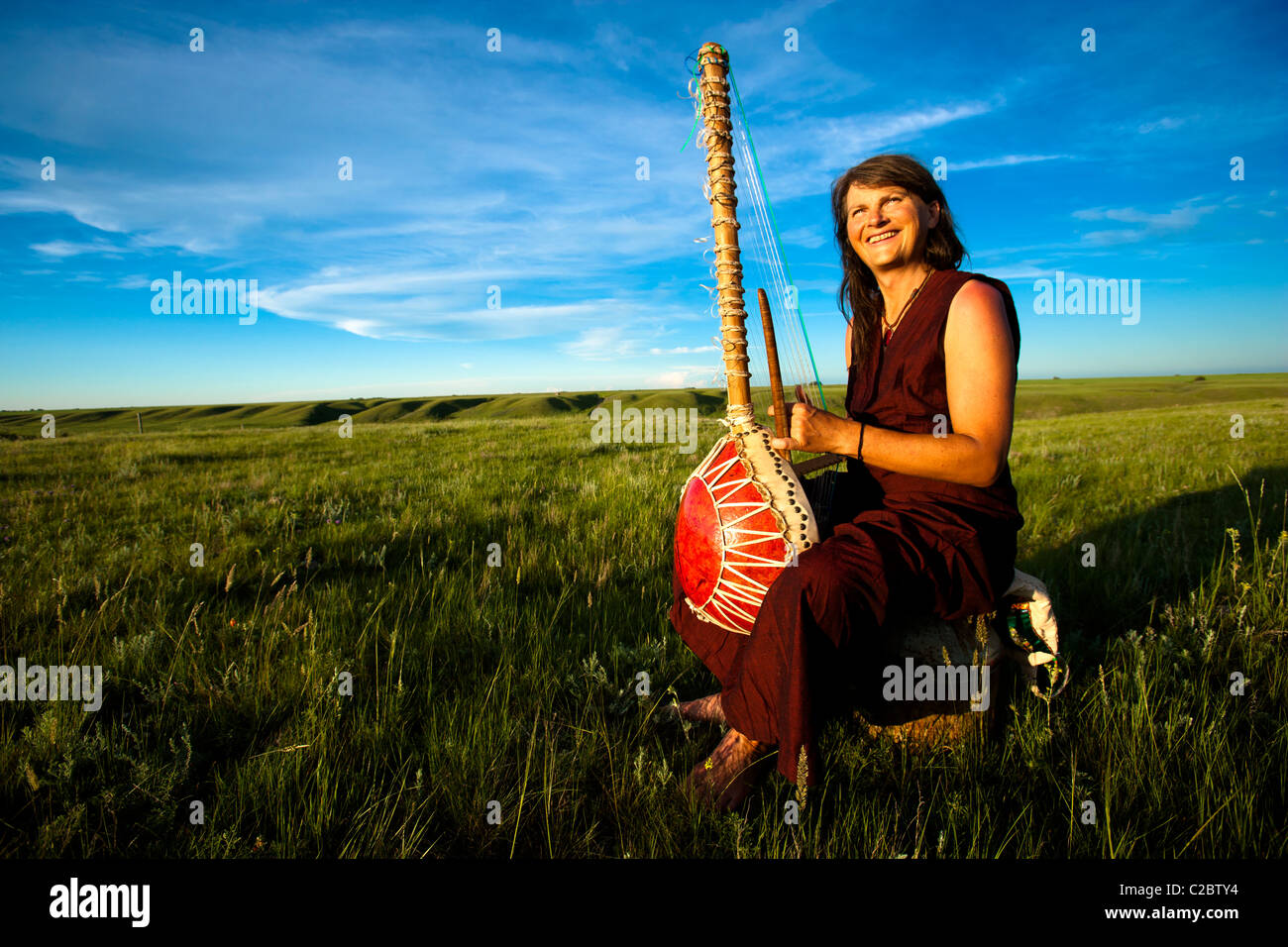 Frau spielt eine handgefertigte Cora (Kora) das Instrument besteht aus einem Kürbis, Elch ausblenden und Bison ausblenden. Stockfoto