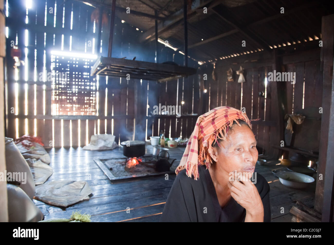 PA-O Indianerin in native Kostüm sitzt in ihrer Shanty-Küche mit offenem Kamin. Samkar, Inle-See, Shan-Staat, Burma. Stockfoto