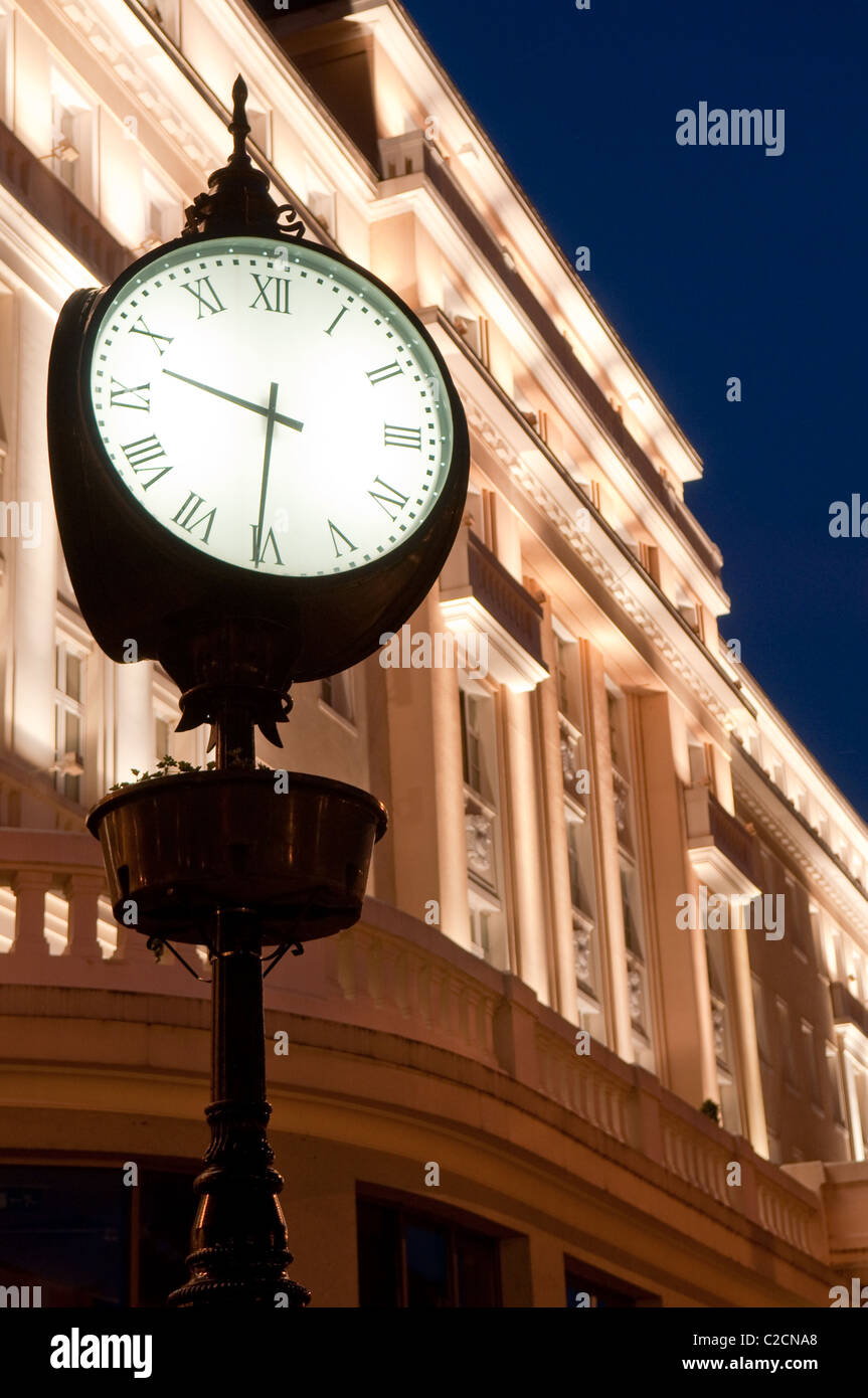 alte Uhr mit Gebäude durch die Lichter im Hintergrund beleuchtet Stockfoto