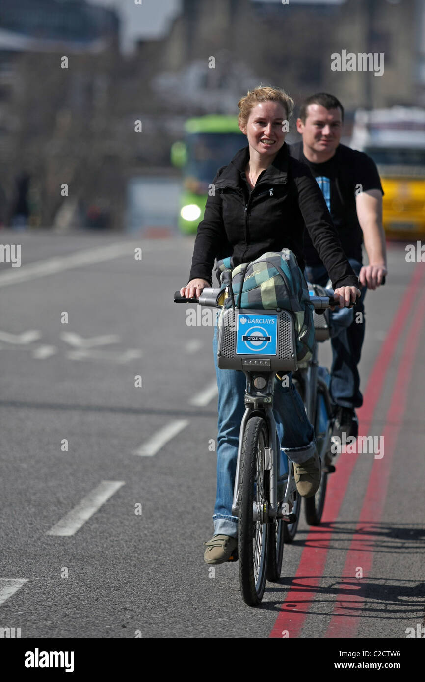 Eine weibliche Radfahrer, Radfahren auf einem Boris Bike vor ein männlicher Radfahrer in London, England Stockfoto