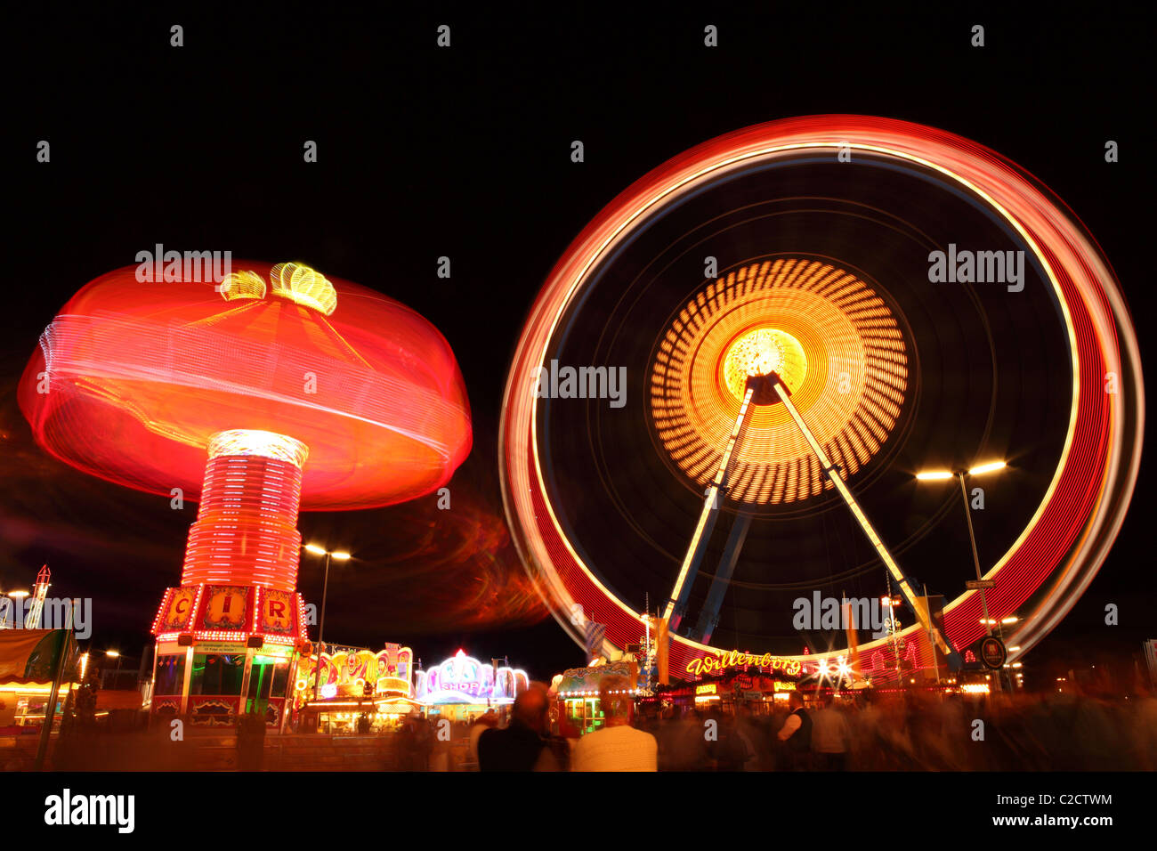 Ein Karussell dreht sich durch das große Rad in der Nacht auf dem Münchner Oktoberfest in Deutschland. Stockfoto