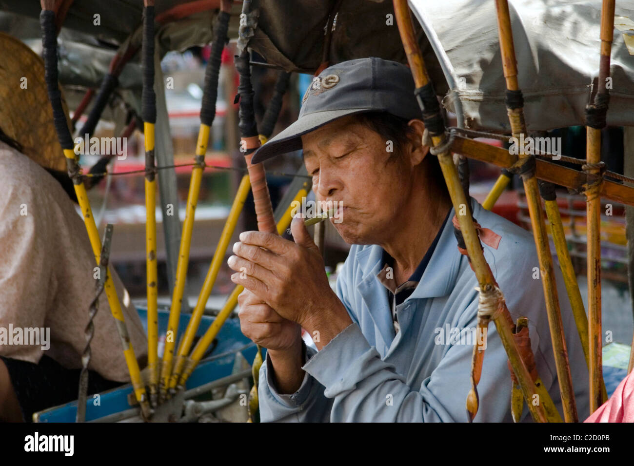 Ein asiatischer Mann mittleren Alters ist eine kleine Zigarre an einem Taxistand in Tachilek, Birma (Myanmar) Beleuchtung. Stockfoto