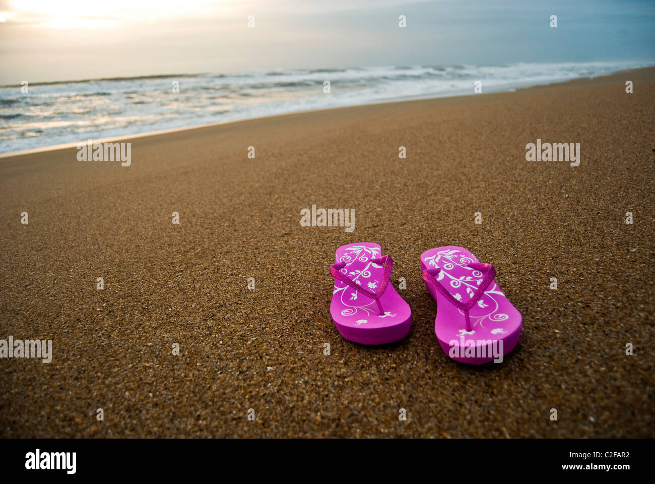 Rosa Damen Flip-flops auf einem leer und sauber Strand bei Sonnenaufgang. Stockfoto