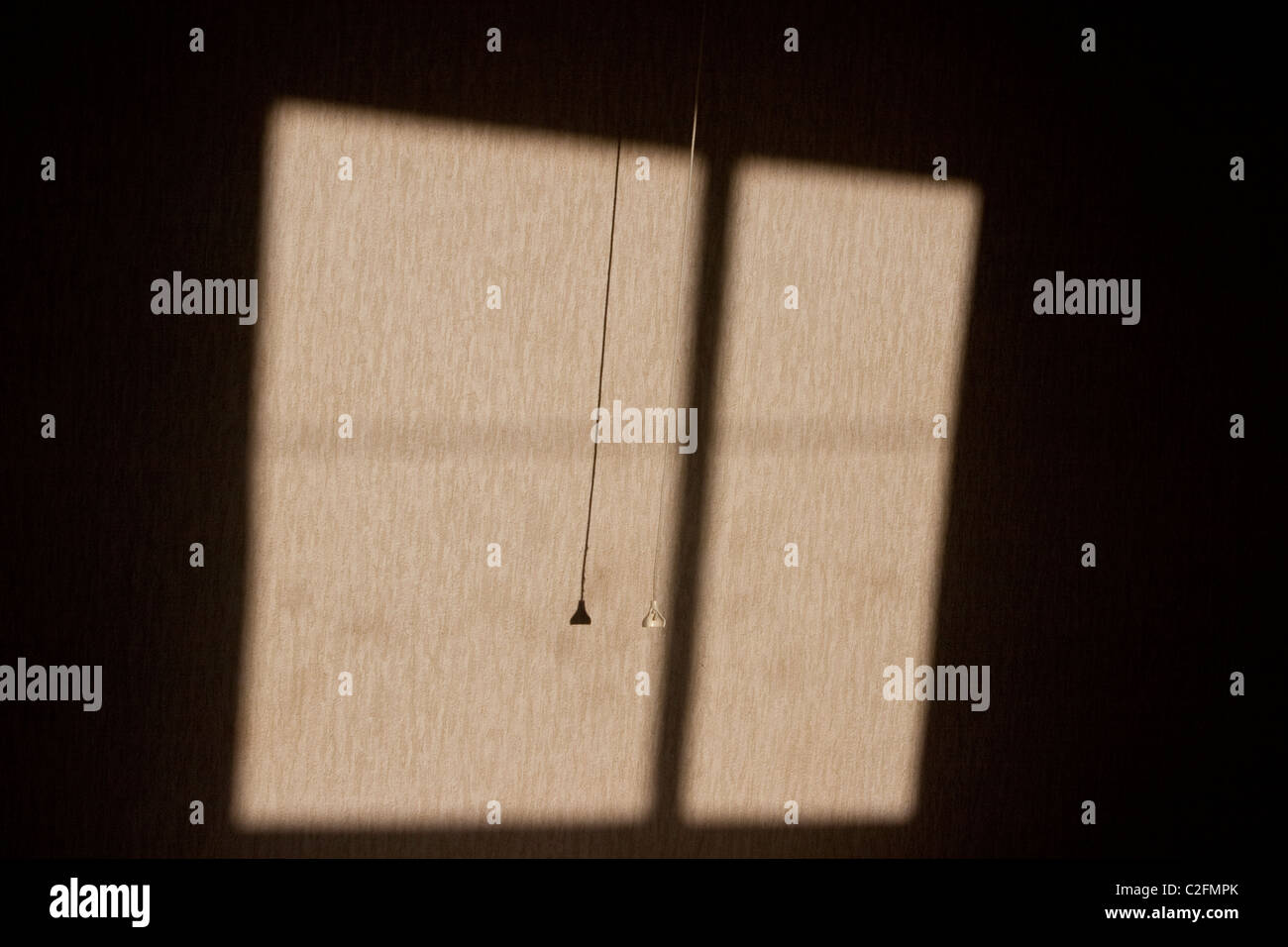 Das ist ein Bild von einem Schatten der Sonne durch ein Schlafzimmerfenster.  Zugschnur ist auch sichtbar und daraus resultierende Schatten Stockfoto