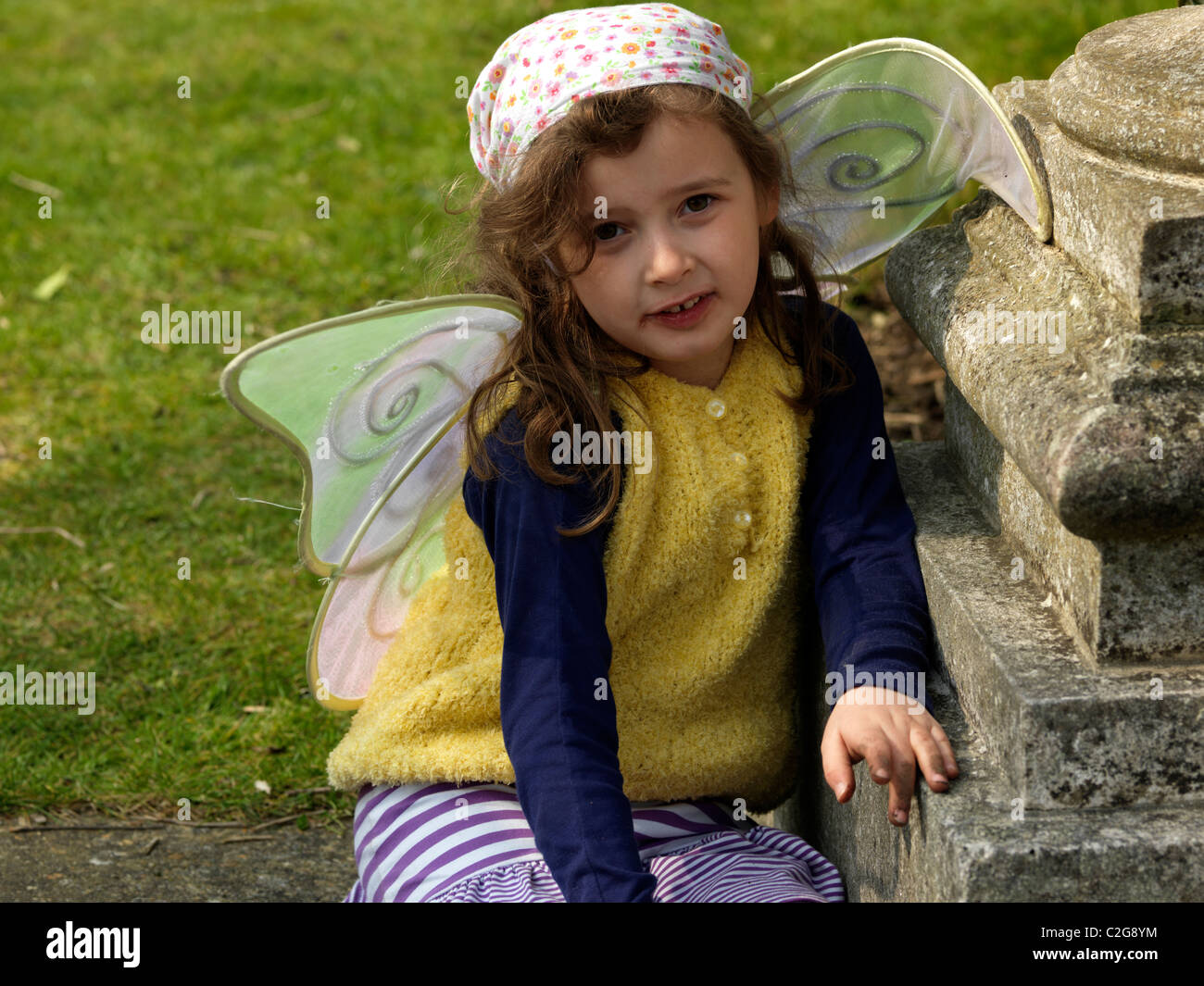 Junge Mädchen Wings Wearing Fee sitzen im Garten Englands Stockfoto