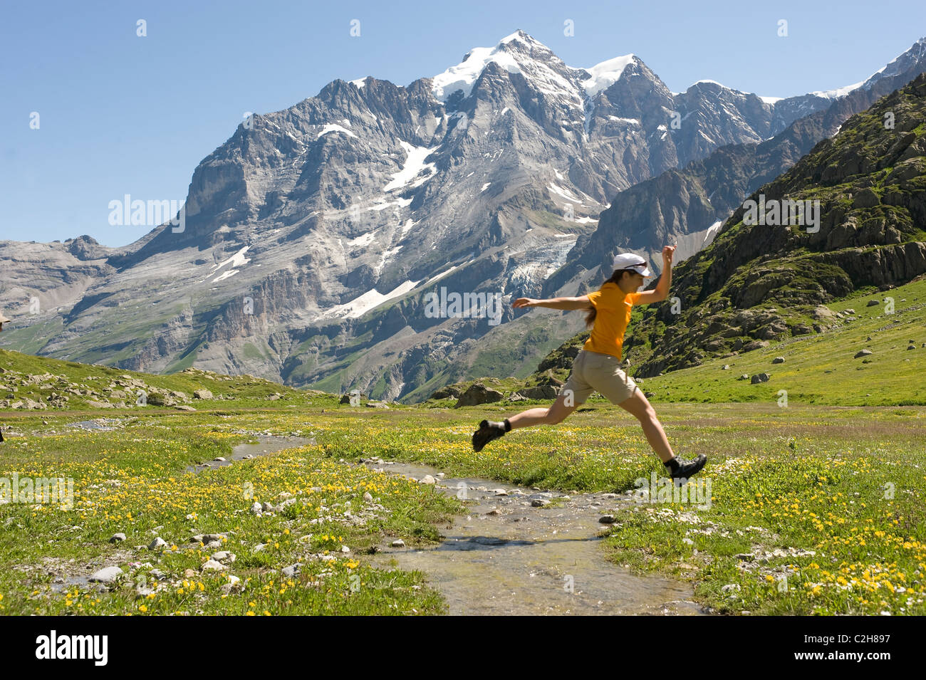 Eine Frau, die einen Sprung über einen Gebirgsbach, sogenannten, Schweiz Stockfoto