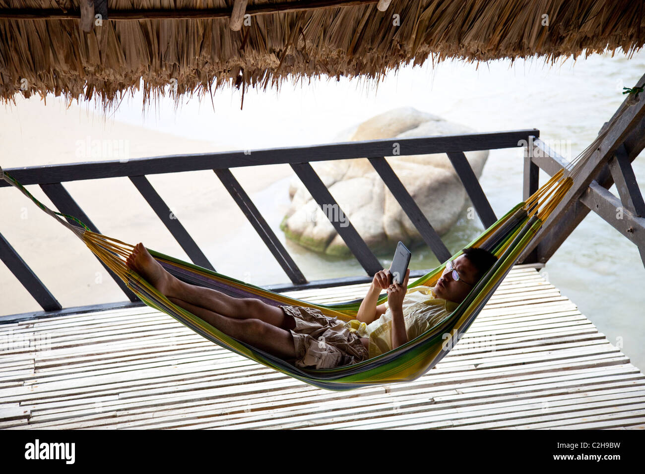 Tourist in einer Hängematte entspannen und lesen einen Kindle direkt am Meer in Kolumbien Stockfoto