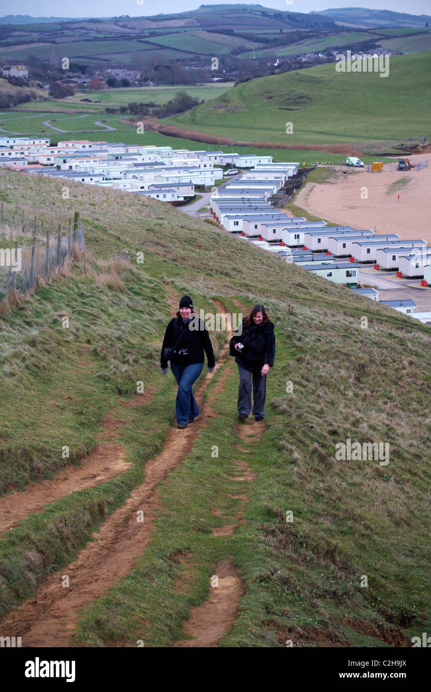 Zwei Frauen mit Kameras, die im Januar in West Bay, Dorset UK, den Berg mit Wohnwagenpark und die umliegende Landschaft hinaufgehen - Wohnwagen Stockfoto