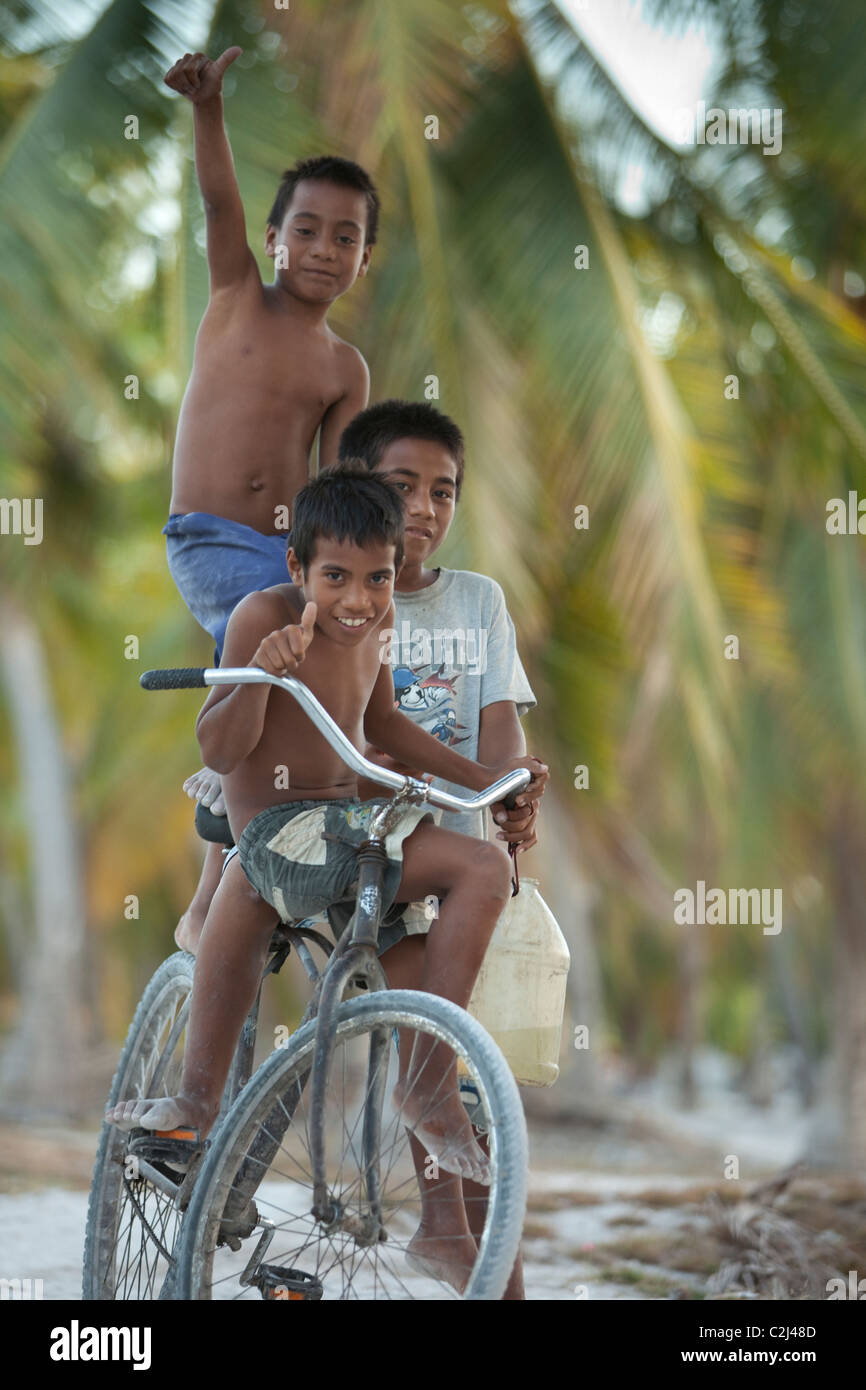 Drei Heimatinsel jungen auf einem Fahrrad unten Insel Coral, Palme gesäumten Straße. Stockfoto