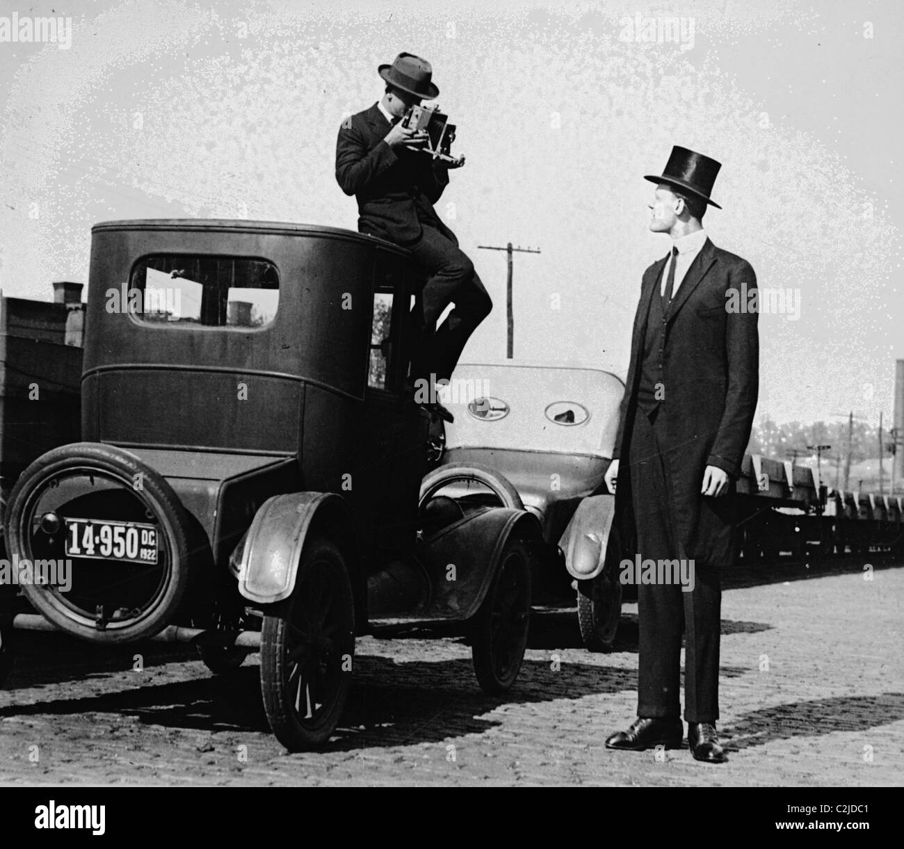 Fotograf Mounts selbst auf dem Dach eines Autos ein Bilder von einem außerordentlich hohen Männer in einen Hut zu schießen. Stockfoto