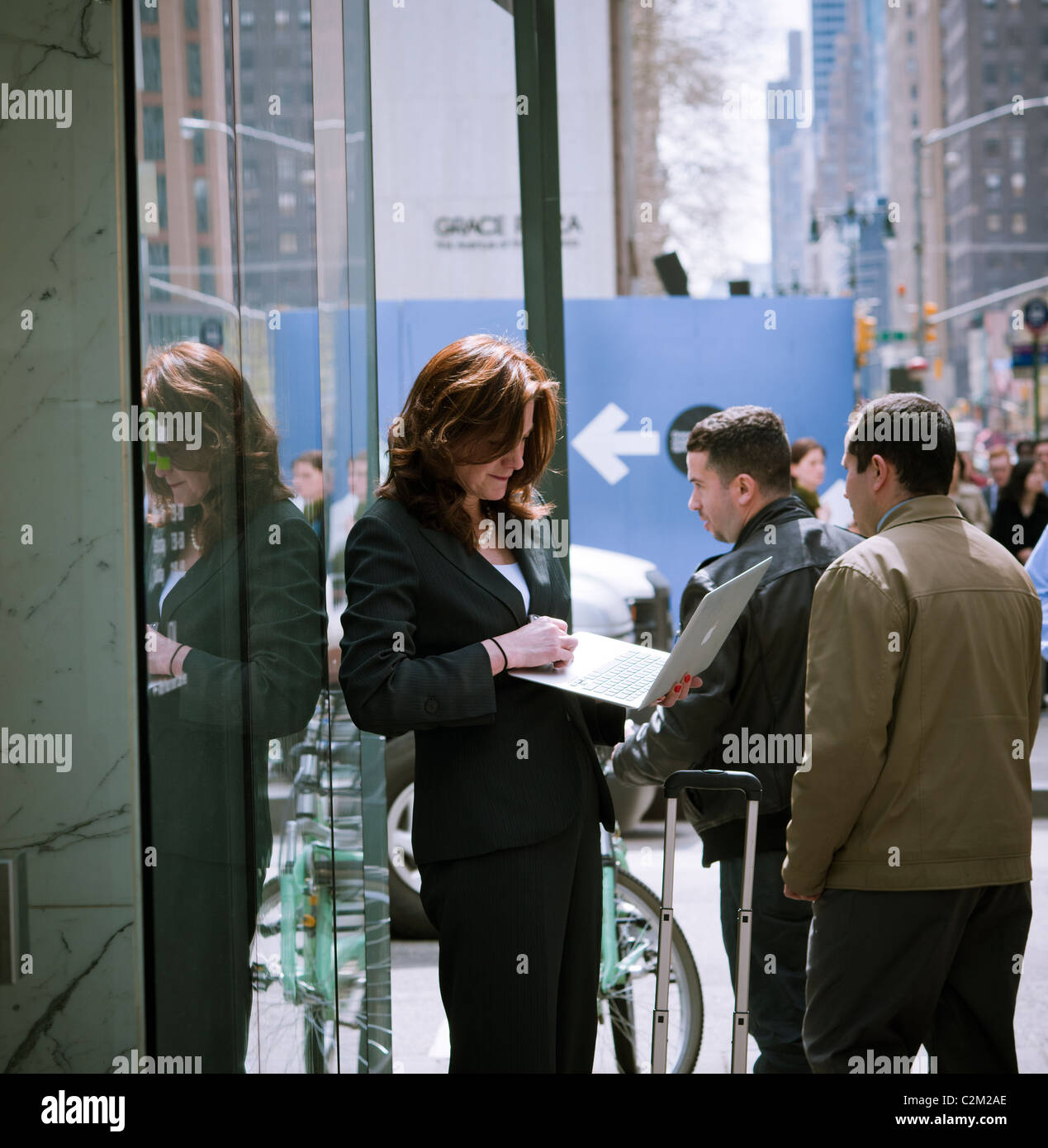 Eine Frau steht vor einem Bürogebäude mit ihrem Macbook Laptop in Midtown Manhattan in New York Stockfoto
