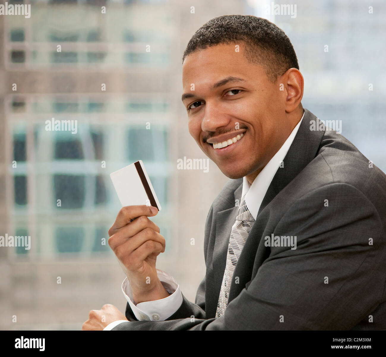 Afrikanische amerikanische Geschäftsmann sitzt in seinem Büro hält eine Kreditkarte Stockfoto