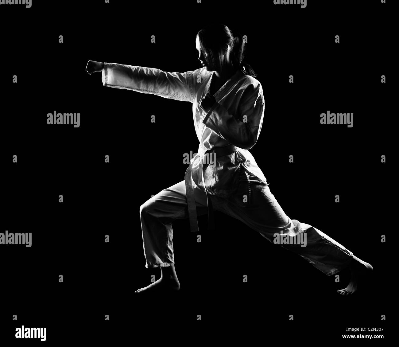 Full-length Silhouette Portrait schöne Martial-Arts-Mädchen im Kimono Excercising Karate Kata auf schwarz Stockfoto
