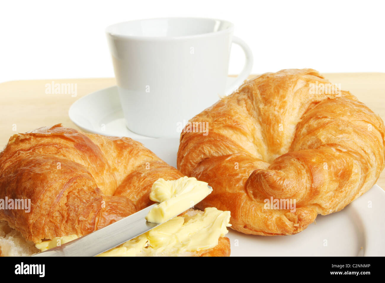Nahaufnahme von Croissants und Butter auf ein Messer mit einer Tasse und Untertasse im Hintergrund Stockfoto