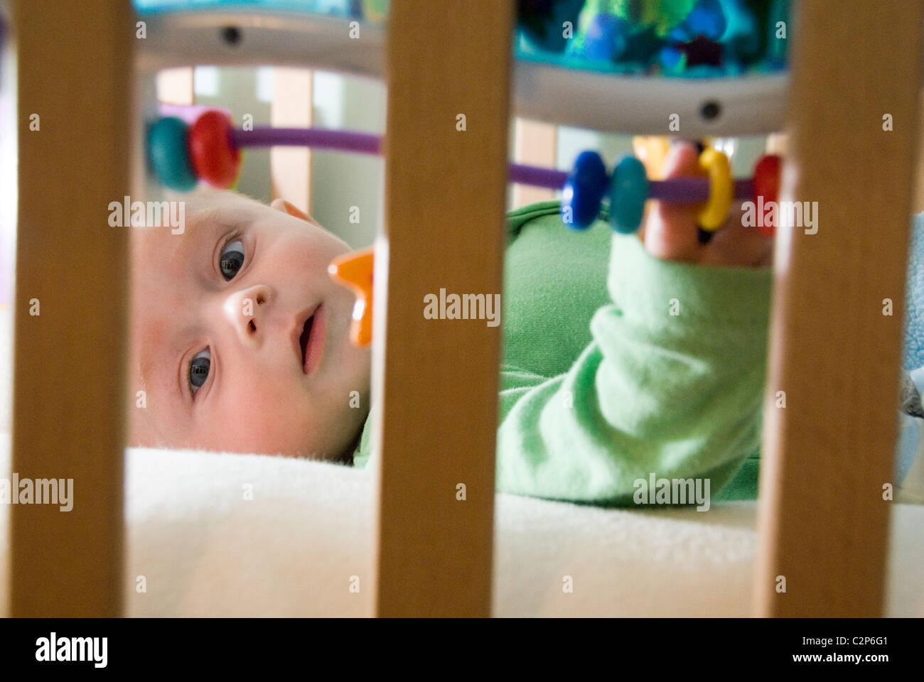 Hautnah am Gesicht des jungen im Bett Kinderbett Bars mit baumelnden Spielzeug durchsehen Stockfoto