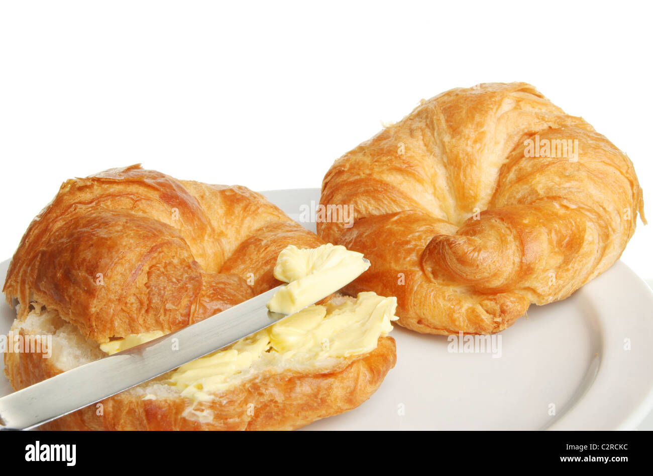 Nahaufnahme von zwei Croissants auf einem Teller mit Butter auf einem Messer Stockfoto
