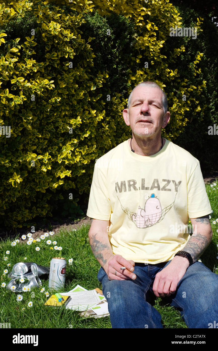 arbeitsloser Mann im öffentlichen Park genießen Sie die Sonne mit Vorteile Broschüren Bier und Zigaretten Stockfoto