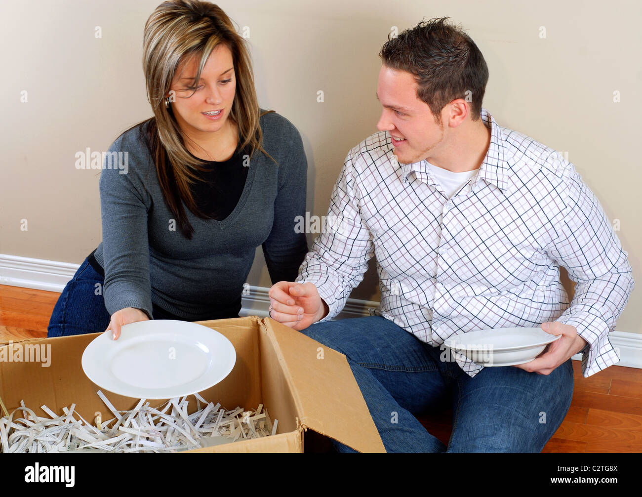 Junges Paar sitzt auf dem Boden Auspacken Boxen In ihrem neuen Zuhause Stockfoto