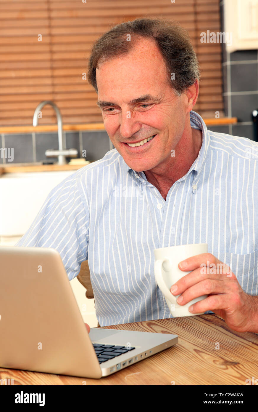 Glücklicher Mann mit seinem Laptop in der Küche hält eine Tasse Tee oder Kaffee Stockfoto