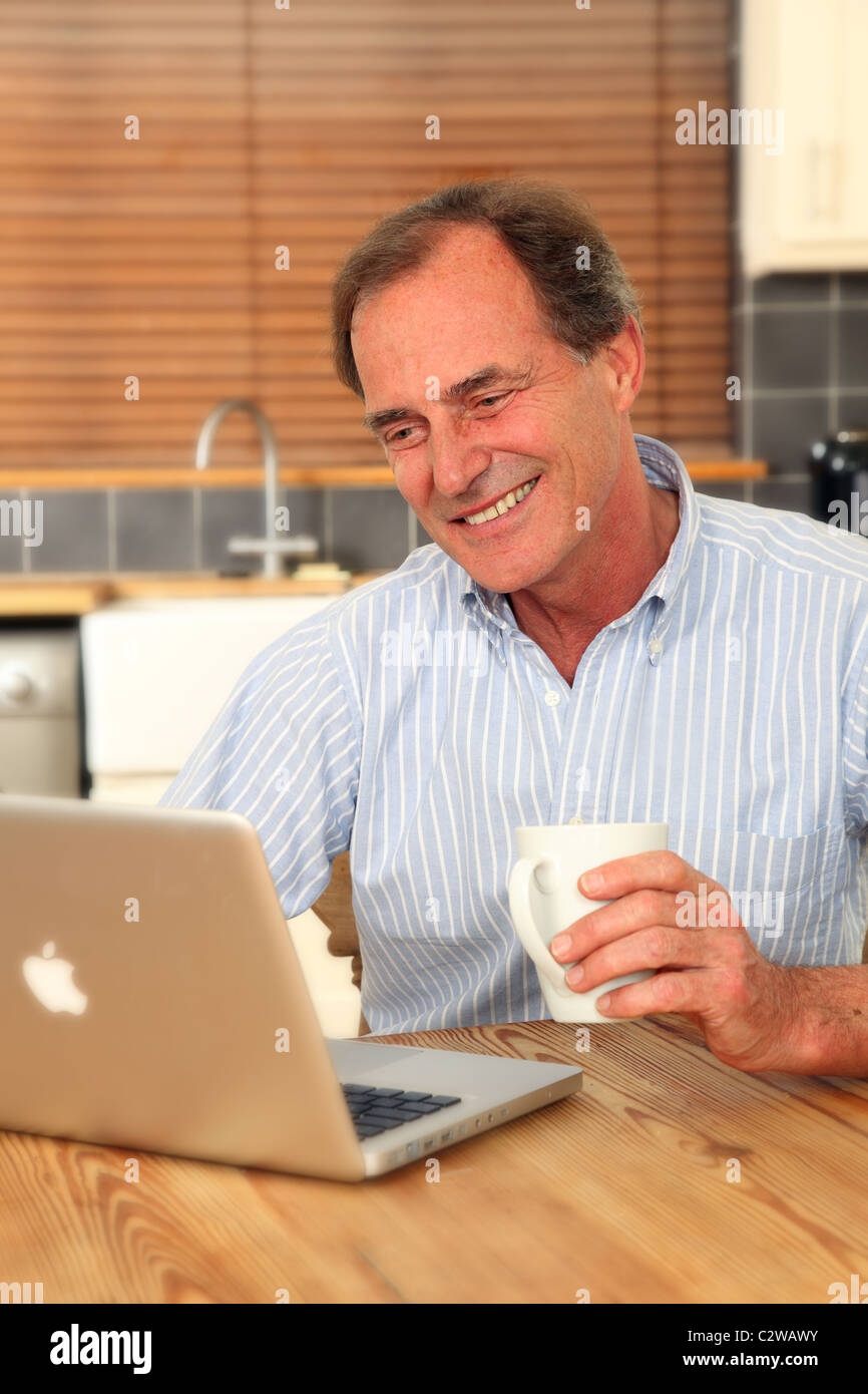 Glücklich reifer Mann mit seinem Laptop in der Küche hält eine Tasse Tee oder Kaffee Stockfoto