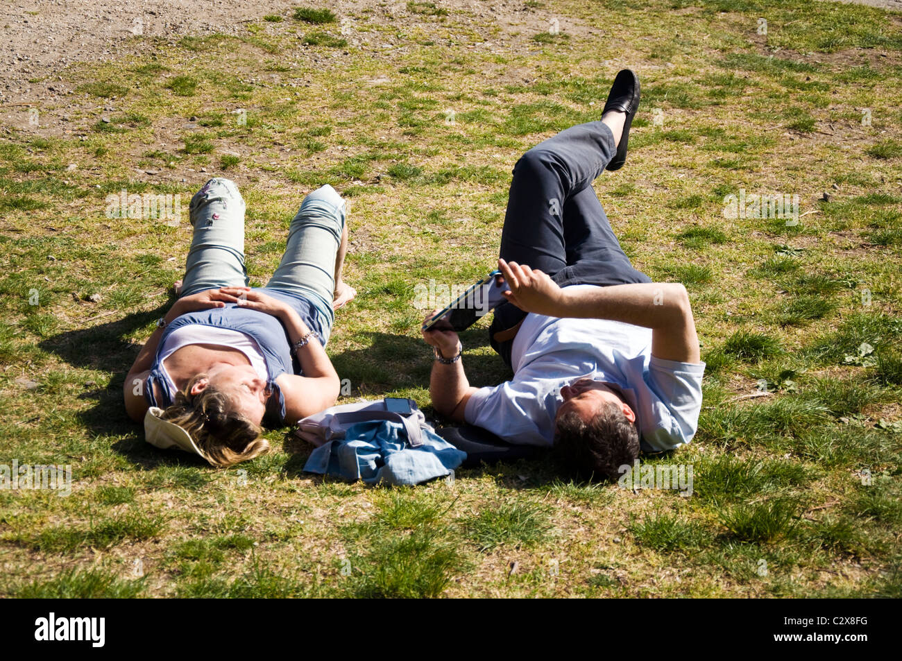 Mann liest einen Roman oder Buch auf einem Tablet-PC mit Frau neben ihm auf dem Rasen liegend Stockfoto
