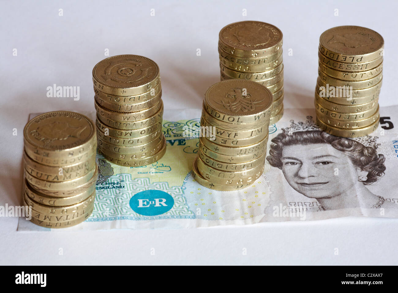 £55-5 Stapel von 10 £1 Münzen gestapelt an der Spitze eine Anmerkung £5 auf weißem Hintergrund Stockfoto