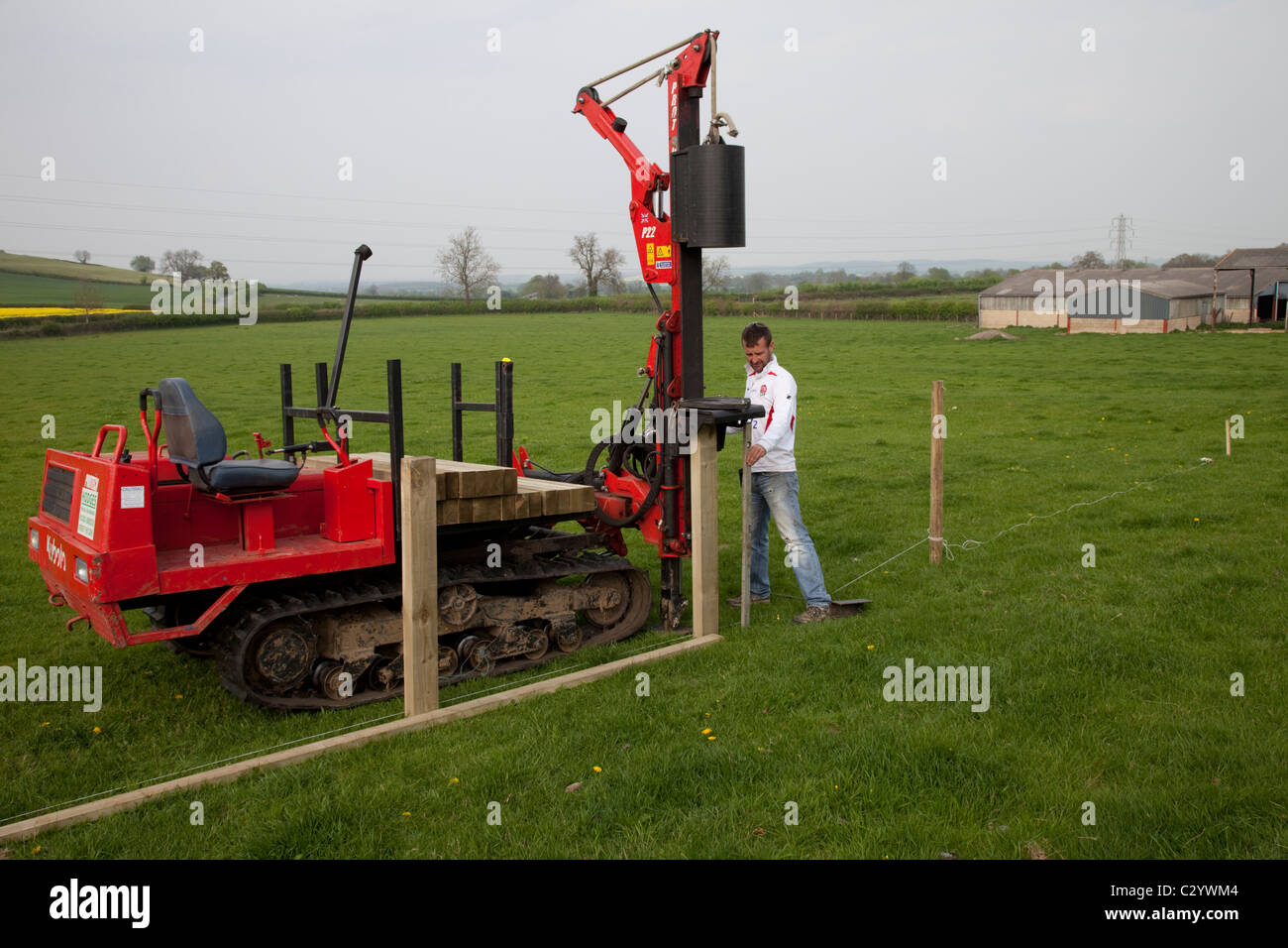 Arbeiter fahren Holz Beiträge in Feld mit Post Stampfer für neue Post und Bahn Weidezaun Cotswolds UK Stockfoto