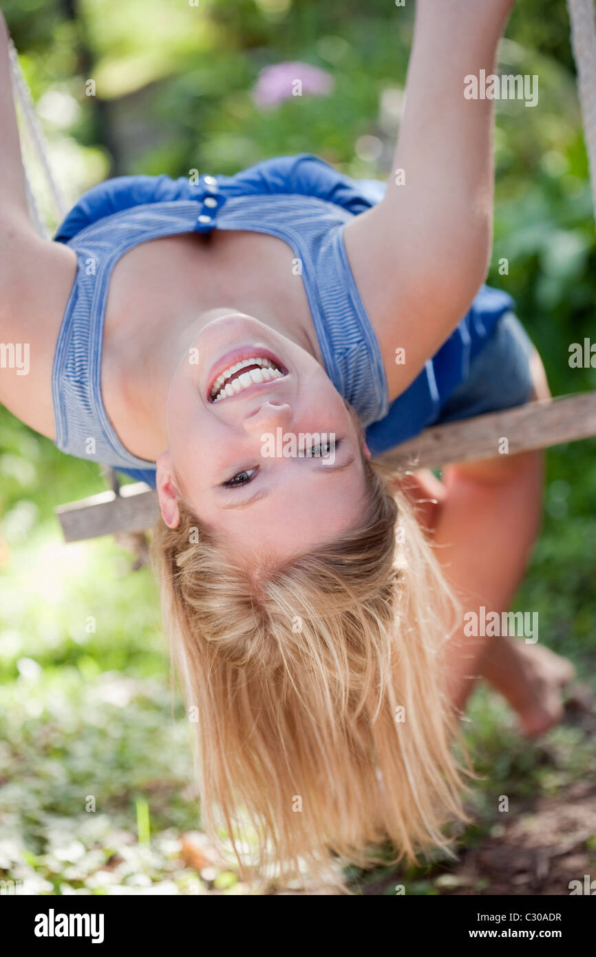 Junge Frau mit einem schönen Lächeln nach hinten gelehnt auf einer Schaukel im Garten Stockfoto