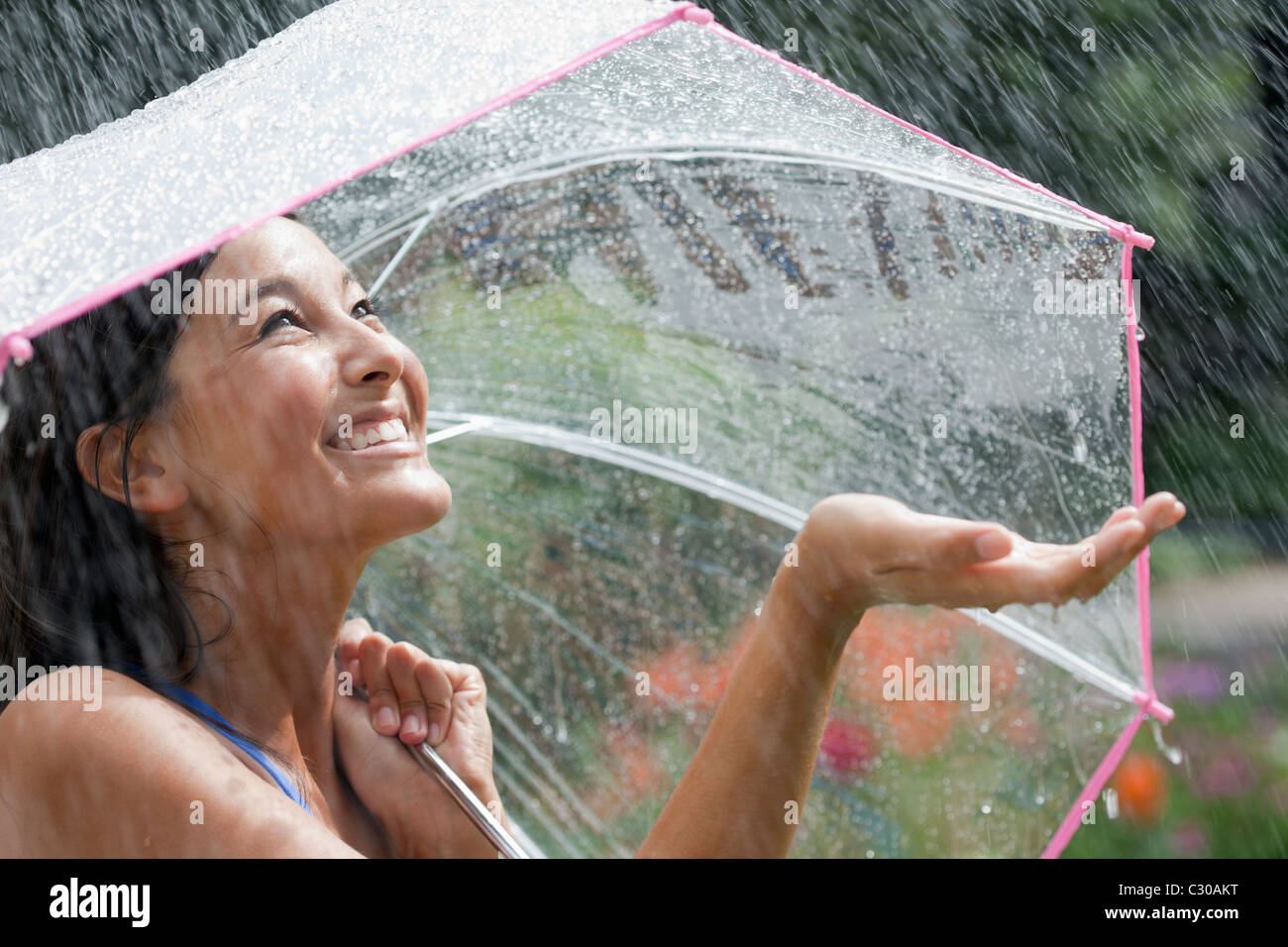 Junge hübsche Asiatin lächelnd im Regen Stockfoto