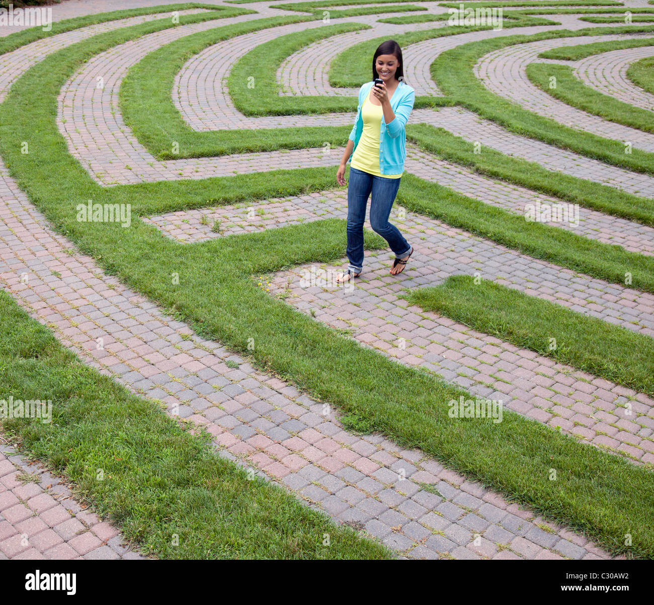 Schöne junge asiatische Frau Lächeln beim Lesen ihres Mobiltelefons und zu Fuß durch ein Labyrinth. Quadratische Schuss. Stockfoto