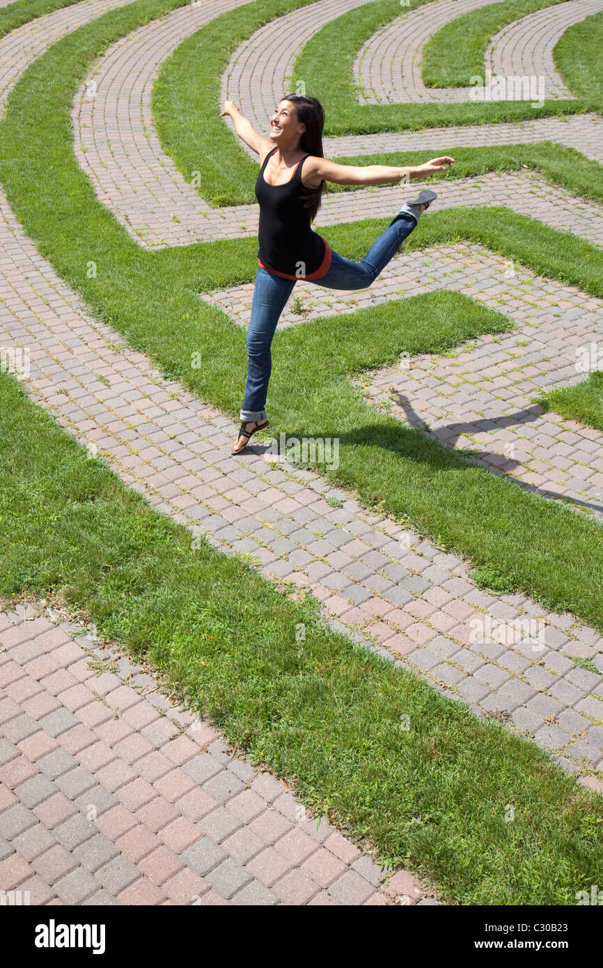 Schöne junge asiatische Frau springt spielerisch über die Grass-Grenze eines Park-Labyrinths. Vertikale erschossen. Stockfoto