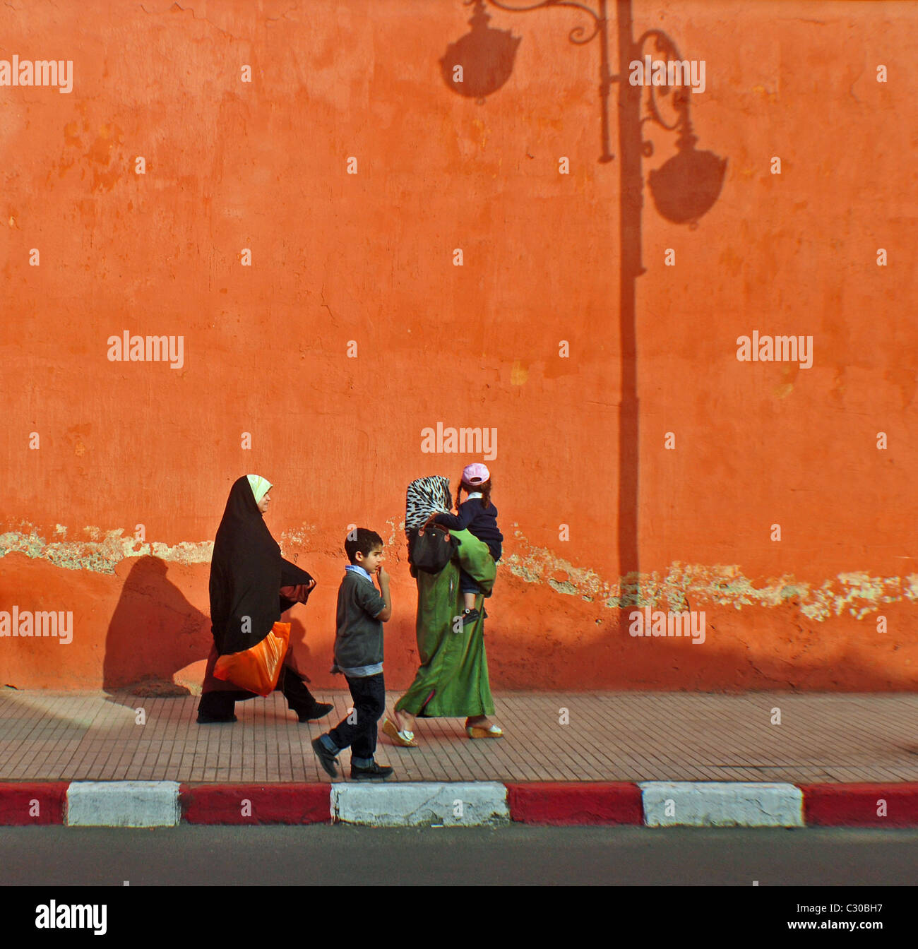 Menschen zu Fuß vorbei an den Schatten von einem Laternenpfahl auf einer farbigen Wand in Marrakesch, Marokko Stockfoto