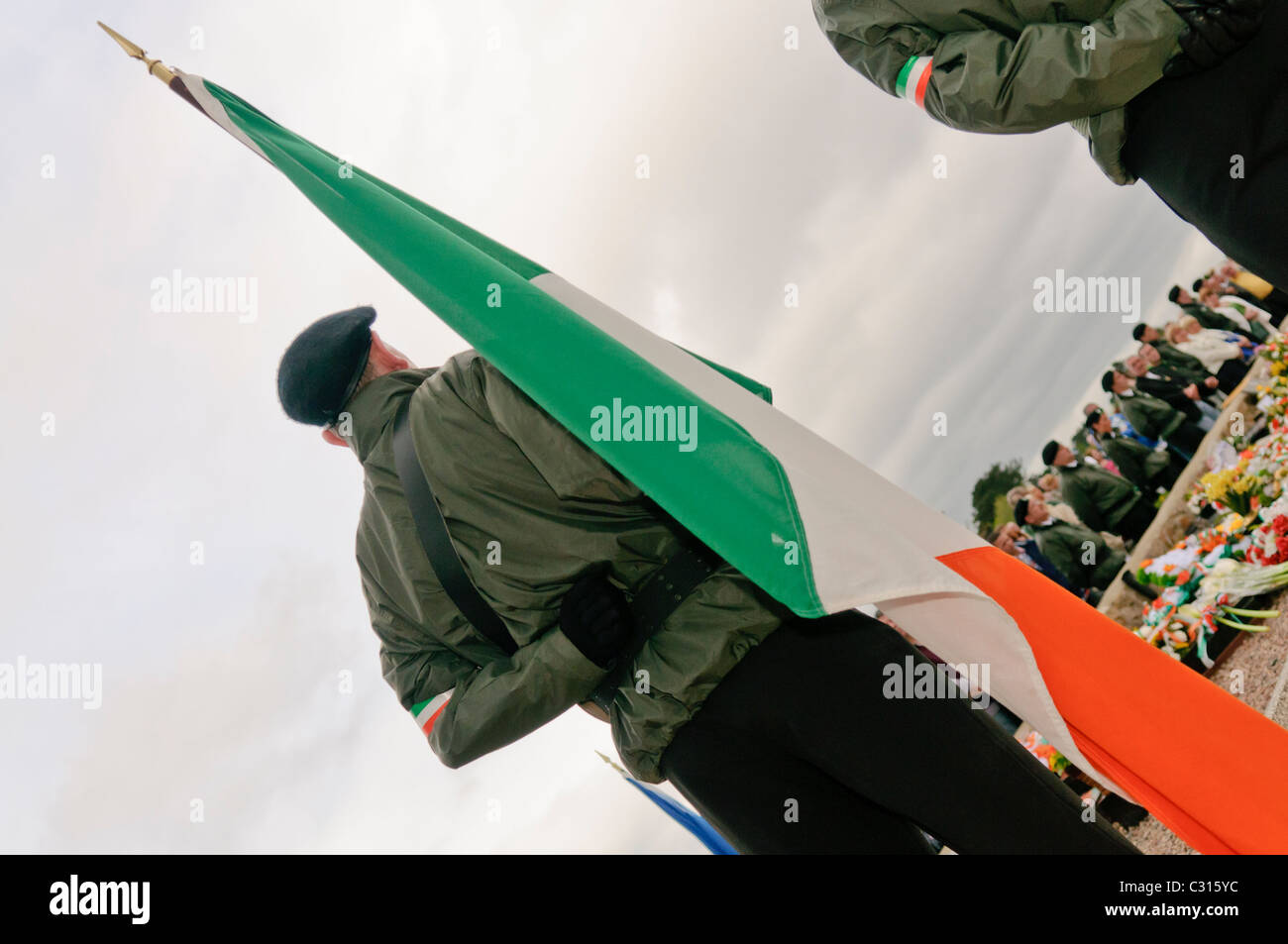 Männer, gekleidet in paramilitärischen Uniformen, und Vertreter der Sinn Féin, der politische Flügel der Irisch-Republikanischen Armee (IRA), halten Sie die Irische trikolore Flaggen während der jährlichen Ostern steigende Gedenken, Belfast, Nordirland. Stockfoto