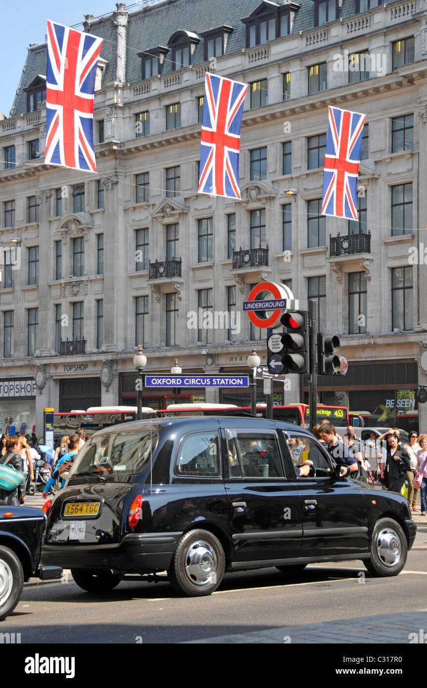 Schwarzes Taxi an der Ampel in der belebten Straßenszene vor dem Oxford Circus London U-Bahnstation Union Jack Decorations England UK Stockfoto