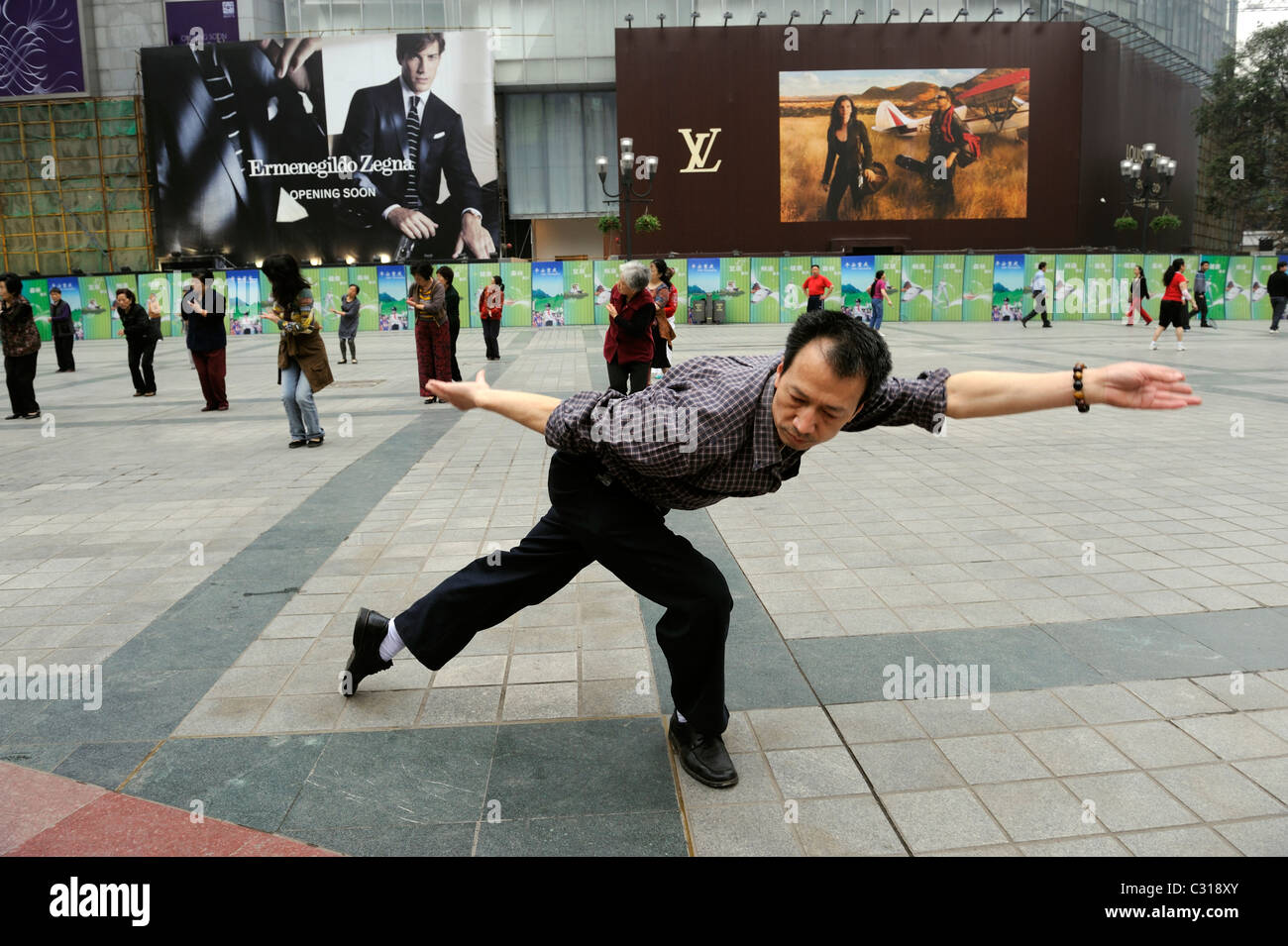 Ein Mann praktiziert Tai Chi vor Louis Vuitton und Ermenegildo Zegana Plakatwände in der Innenstadt von Chongqing, China. 22. April 2011 Stockfoto