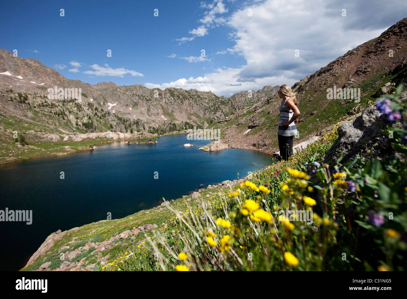 Eine junge Frau steht auf einem Berghang mit Blick auf einen Bergsee in Colorado Wildblumen bedeckt. Stockfoto